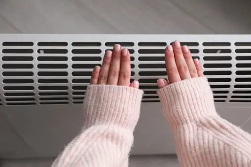 lady holding hand by heat vent